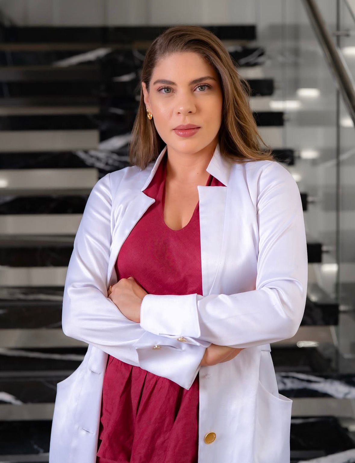 La Dra. Katherine Cuentas Pacheco, dermatóloga, con bata blanca sobre vestido vino, en su consultorio.